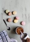 From above anonymous person pouring milk into cup of coffee near bunch of colorful macaroons and spoon — Stock Photo