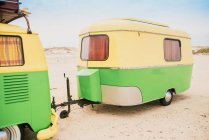 Барвистий мікроавтобус з трейлером, припаркований на піщаному березі в сонячний день — стокове фото