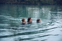Средняя взрослая женщина с маленькими детьми плавает в теплой воде пруда, проводя время в открытом спа — стоковое фото