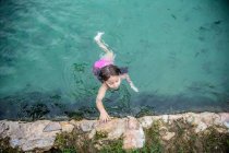 Зверху маленька дівчинка плаває до кам'яної межі в теплій воді відкритого басейну, відпочиваючи в спа-центрі — стокове фото