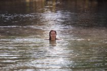 Mujer adulta mirando en cámara mientras nada en agua tibia limpia de estanque en spa y disfruta de sol durante el día - foto de stock
