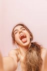 Portrait of a teenage girl making a selfie with expression of happiness on pink background — Stock Photo