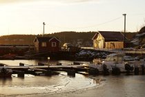 Wharf and boat on waterfront covered with ice beside frosty shore with cottages — Stock Photo