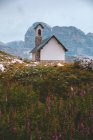 Bâtiment blanc et gris sur colline rocheuse avec herbe verte épaisse contre de belles montagnes brumeuses dans les Dolomites par temps couvert — Photo de stock