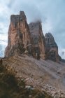 Incredibile vista dai piedi con erba verde e piccole rocce di cime nebbiose delle montagne Drei Zinnen nelle Dolomiti durante il tempo coperto — Foto stock
