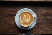De cima xícara de cappuccino fresco com forma de coração na espuma servida na mesa de madeira no café — Fotografia de Stock