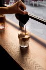 Официант-земледелец наливает свежий кофе в стакан со льдом молока на деревянный прилавок у окна в кафе — стоковое фото