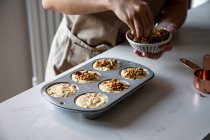 Cultivez la personne en tablier saupoudrer de cupcakes crus faits maison dans un plat de cuisson avec des noix écrasées dans la cuisine — Photo de stock