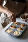 Обрізати людину в фартусі, посипаючи сирі домашні кекси у випічці тарілки з подрібненими горіхами на кухні — стокове фото