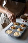 Persona de la cosecha en delantal espolvorear cupcakes caseros crudos en bandeja para hornear con nueces trituradas en la cocina - foto de stock