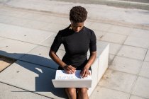 Konzentrierte Afroamerikanerin im eleganten schwarzen Kleid mit Laptop auf dem Bürgersteig — Stockfoto