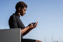 Seitenansicht einer konzentrierten afrikanisch-amerikanischen Frau im eleganten schwarzen Kleid per Mobiltelefon — Stockfoto
