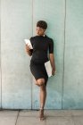 Крутая афро-американская умная женщина с помощью мобильного телефона, держащего ноутбук, опираясь на бетонную стену — стоковое фото