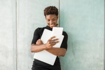 Cool African American smart woman taking selfie while holding a laptop standing leaning on concrete wall — Stock Photo