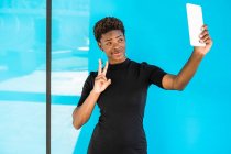 Cool afro-américaine femme intelligente prenant selfie et montrant le signe v sur fond bleu — Photo de stock