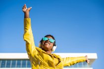 Low angle of happy African American woman in stylish bright jacket and sunglasses jumping with hands up — Stock Photo
