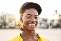 Portrait of happy African American woman in stylish bright jacket looking in camera on sandy beach blurred background — Stock Photo