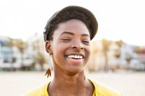 Portrait of happy African American woman in stylish bright jacket with eyes closed on sandy beach blurred background — Stock Photo