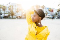 Портрет афроамериканской женщины в стильной яркой куртке, смотрящей в сторону песчаного пляжа размытый фон — стоковое фото