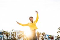 Happy African American woman in stylish bright jacket jumping with hands up on white background — Stock Photo