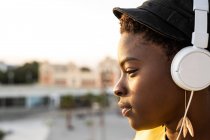 Seitenansicht einer afrikanisch-amerikanischen Frau mit Kopfhörern, die sich auf einen gläsernen Balkon lehnt und vor verschwommenem Hintergrund wegschaut — Stockfoto