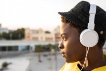 Side view of African American woman in headphones leaning on glass balcony and looking away on blurred background — Stock Photo