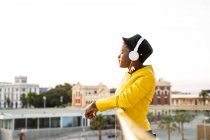 Side view of African American woman in trendy jacket leaning on glass balcony and looking away on blurred background — Stock Photo