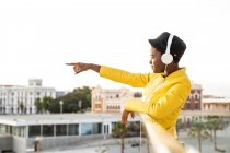 Side view of African American woman in trendy jacket looking away and pointing with finger on blurred background — Stock Photo