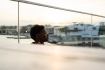 Selective focus side view of serene African American woman chilling on glass balcony and looking away — Stock Photo