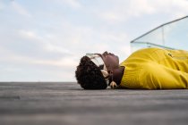 Side view of stylish African American female in modern jacket relaxing on wooden floor and looking away — Stock Photo