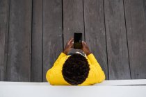 Вид сверху неузнаваемой чернокожей женщины, опирающейся на стену во время использования мобильного телефона — стоковое фото