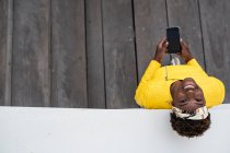 Top view of modern African American woman leaning on wall of modern building while using mobile phone — Stock Photo