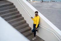 Высокий угол обзора радостной афроамериканки в стильной одежде, чиллирующей на лестнице и отводящей взгляд — стоковое фото
