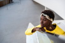 Hohe Winkel der frohen afrikanisch-amerikanischen Frau in stylischer Kleidung chillt auf Treppen, lehnt am Geländer und schaut weg — Stockfoto