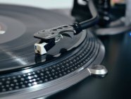 Closeup of top of old black turntable with tonearm maintaining position of cartridge tracing groove and playing LP record — Stock Photo