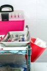 Boîte en plastique rose pour transporter des chats et des outils médicaux sur un plateau chirurgical par mur carrelé dans une clinique vétérinaire — Photo de stock