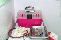 Boîte en plastique rose pour transporter des chats et des outils médicaux sur un plateau chirurgical par mur carrelé dans une clinique vétérinaire — Photo de stock
