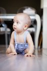 Eccitato bambino a piedi nudi guardando lontano mentre seduto su parquet vicino a banchi in cucina accogliente a casa — Foto stock