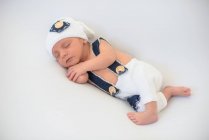 Очаровательный новорожденный ребенок в шляпе и брюках мирно спит на мягком белом матрасе дома — стоковое фото