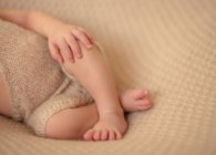 Imagem cortada de bebê descalço deitado cruzou a perna em lençol branco e dormir em casa — Fotografia de Stock
