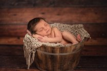 Criança nua em balde no chão de madeira em casa — Fotografia de Stock