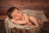 Nude infant in bucket on wooden floor at home — Stock Photo