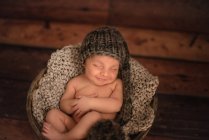 Criança nua em chapéu de malha dormindo em balde no chão de madeira em casa — Fotografia de Stock