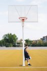 Молодой человек опирается на столб на баскетбольной площадке на открытом воздухе . — стоковое фото