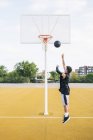 Jeune homme jetant la balle tout en jouant sur le terrain de basket en plein air . — Photo de stock