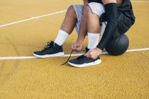 Giovane sul campo da basket fissaggio lacci delle scarpe . — Foto stock