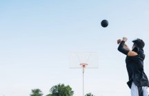 Молодий чоловік кидали м'яч під час гри на баскетбольному майданчику на відкритому повітрі. — стокове фото