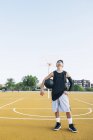 Young man standing with black ball on yellow basketball court outdoors. — Stock Photo