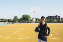 Молодий чоловік стоїть з чорним м'ячем на жовтому баскетбольному майданчику на вулиці . — стокове фото