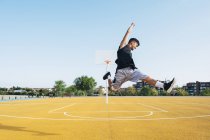 Young man jumping with black ball on yellow basketball court outdoors. — Stock Photo